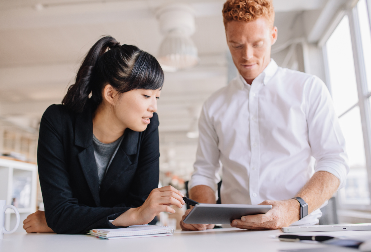 Woman and man in an office, smiling and looking at a tablet.