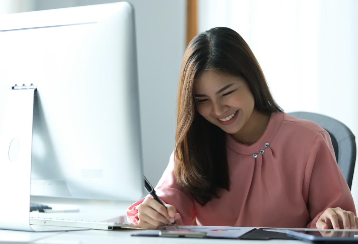 Woman in an office, smiling and looking at a monitor.