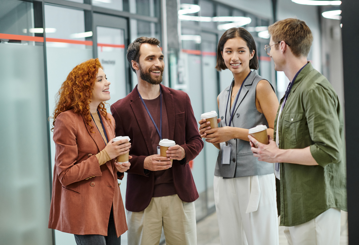 Group of professionals in an office chatting, holding beverage cups.