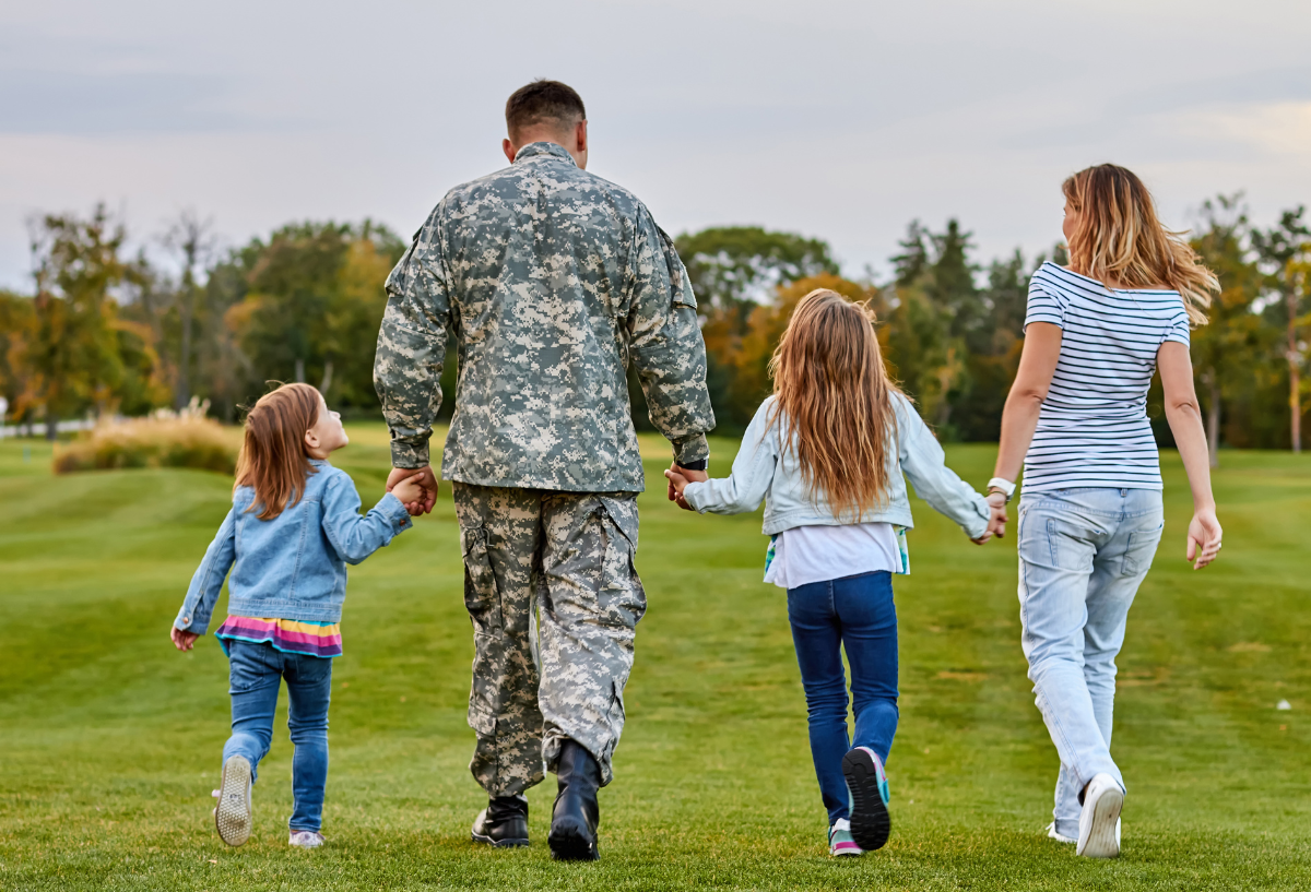 Man in military uniform walking with two children and spouse in a field.