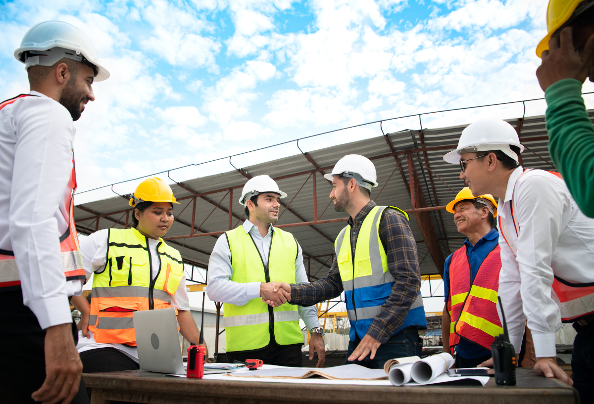 Group of construction workers in hard hats and vests at an outdoor site.