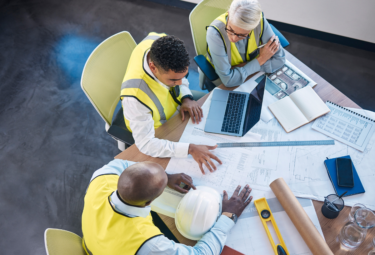 Workers in a yellow hard hat reviewing documents with another person.