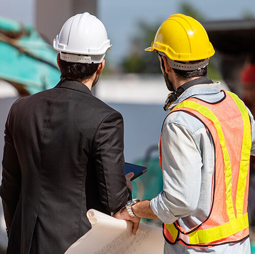 Workers in hard hats on a construction site, seen from behind.