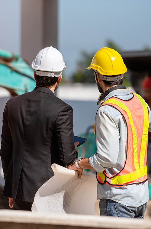 Workers in hard hats on a construction site, seen from behind.