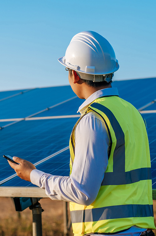 Construction worker in a blue vest and hard hat using a tablet.