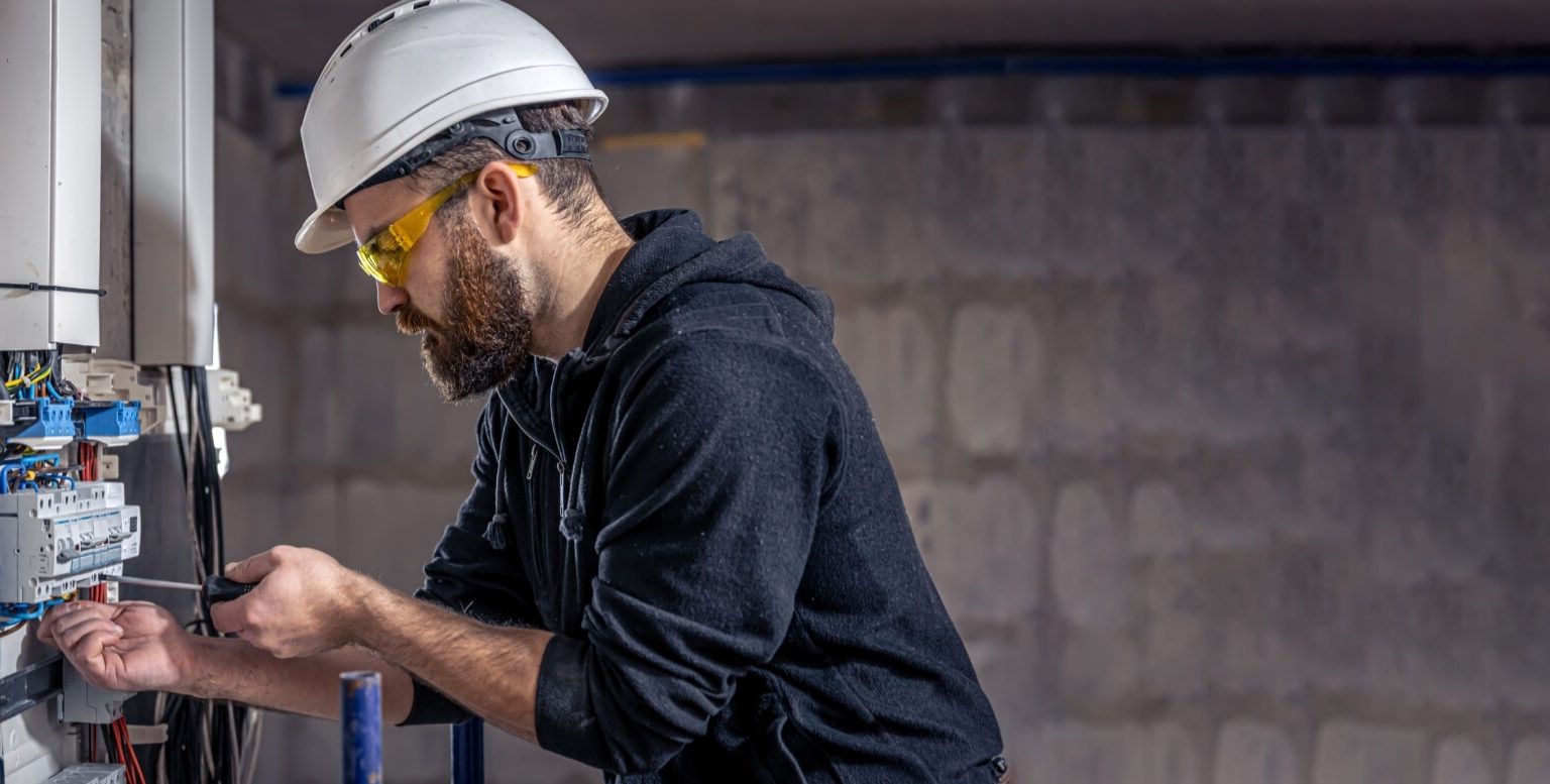 Close-up of a worker in a white hard hat wiring an electrical panel.