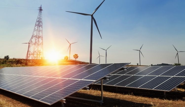 Wind turbines and solar panels in a field during sunrise.
